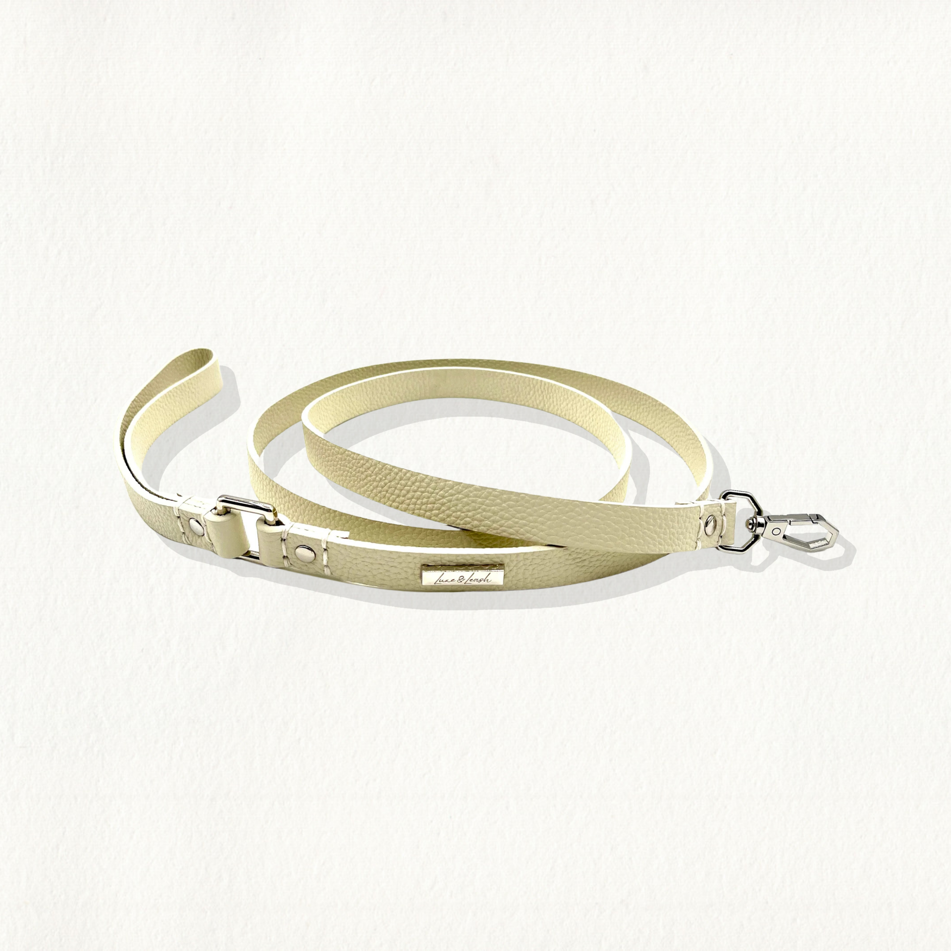 A beige, pebble-textured leather dog leash with gold hardware and a "Luxe & Leash" logo plate, coiled on a white background.
