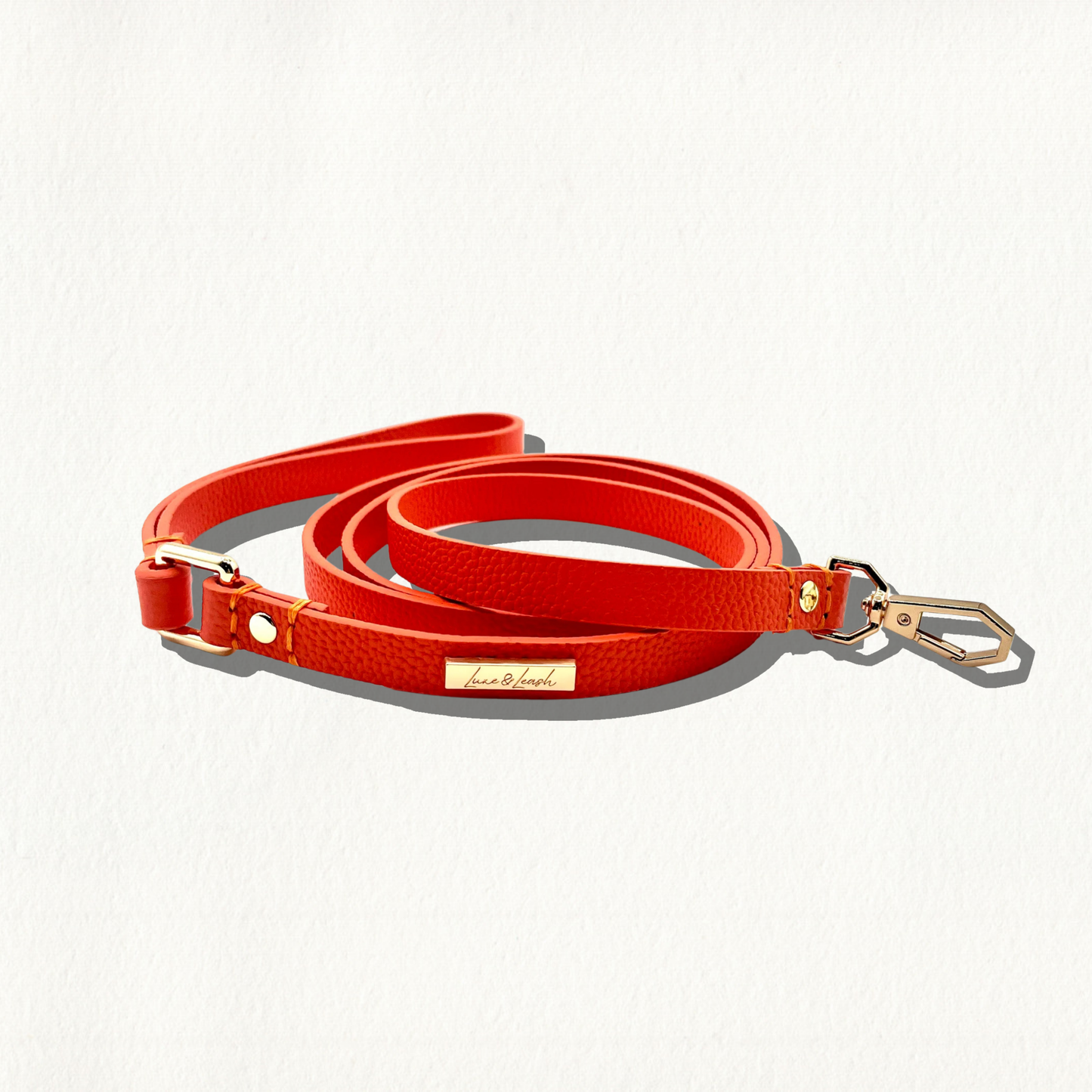 A vibrant orange, pebble-textured leather dog leash with gold hardware and a "Luxe & Leash" logo plate, coiled on a white background.