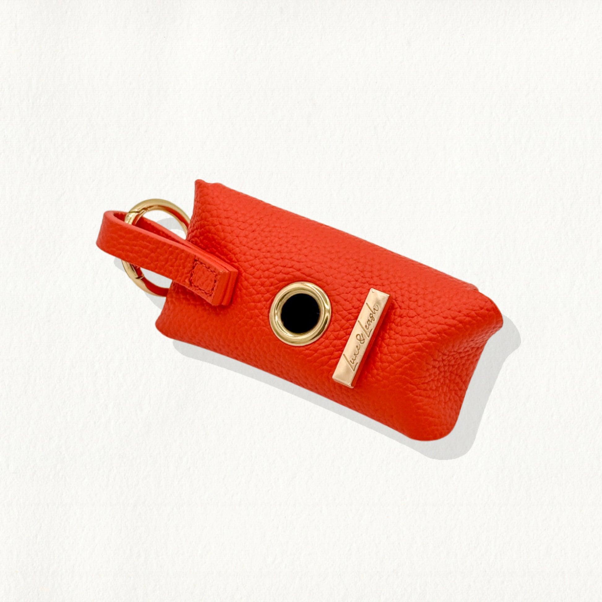 Tangerine leather waste bag dispenser with a gold-rimmed dispensing hole.