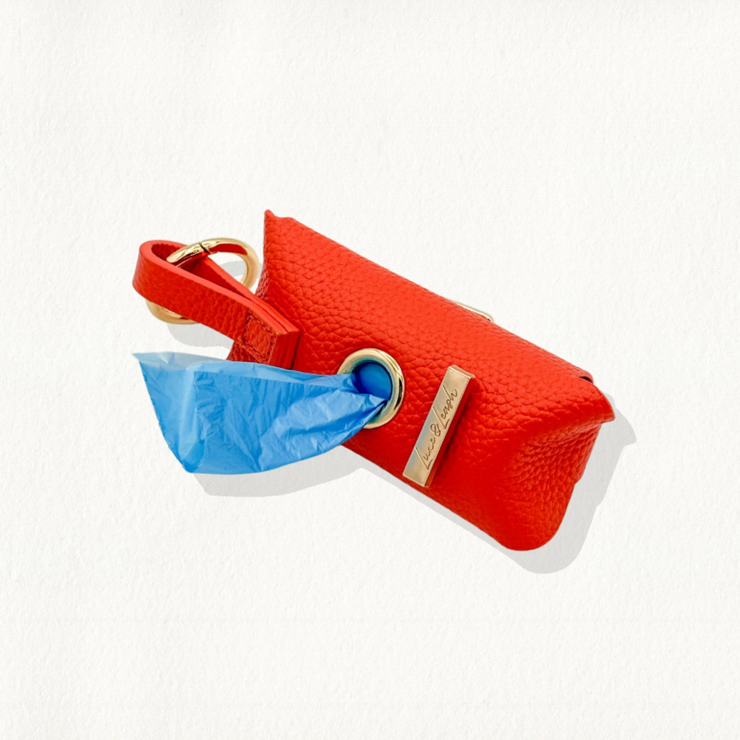 Tangerine leather waste bag dispenser with gold hardware and a "Luxe & Leash" metal bar.