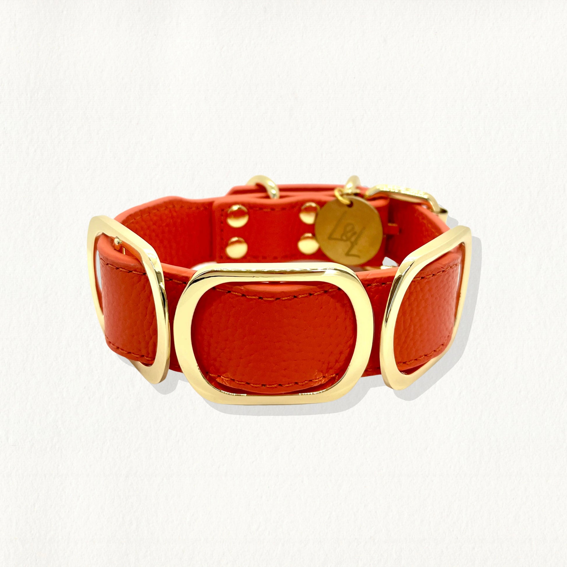a vibrant orange luxury dog collar with a bold, contemporary design. The collar is crafted from high-quality, pebbled leather and is adorned with large, polished gold-toned hardware.