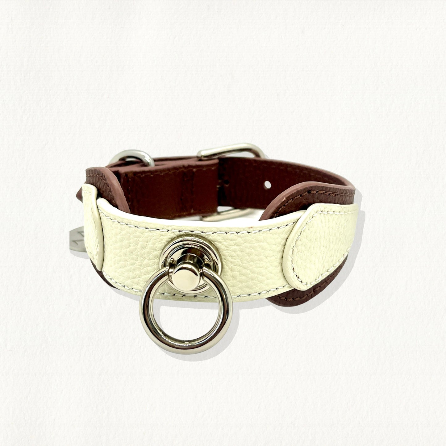 Angled view of a white and brown leather dog collar with a prominent silver-toned metal ring on the front.